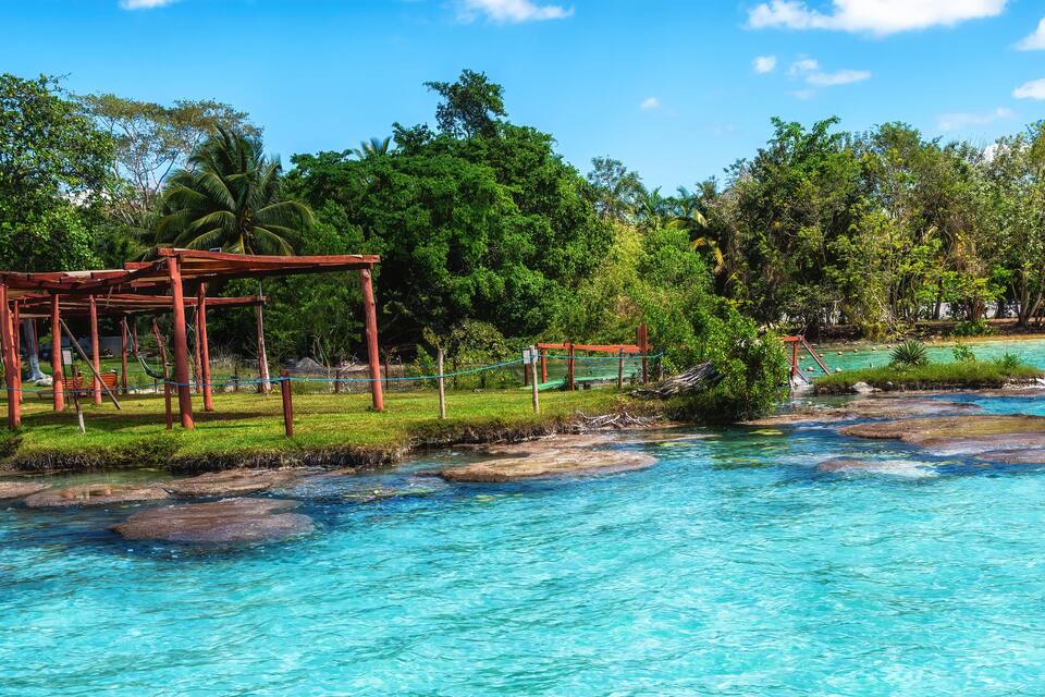 A tropical beach with clear turquoise water, palm trees, and a wooden structure.