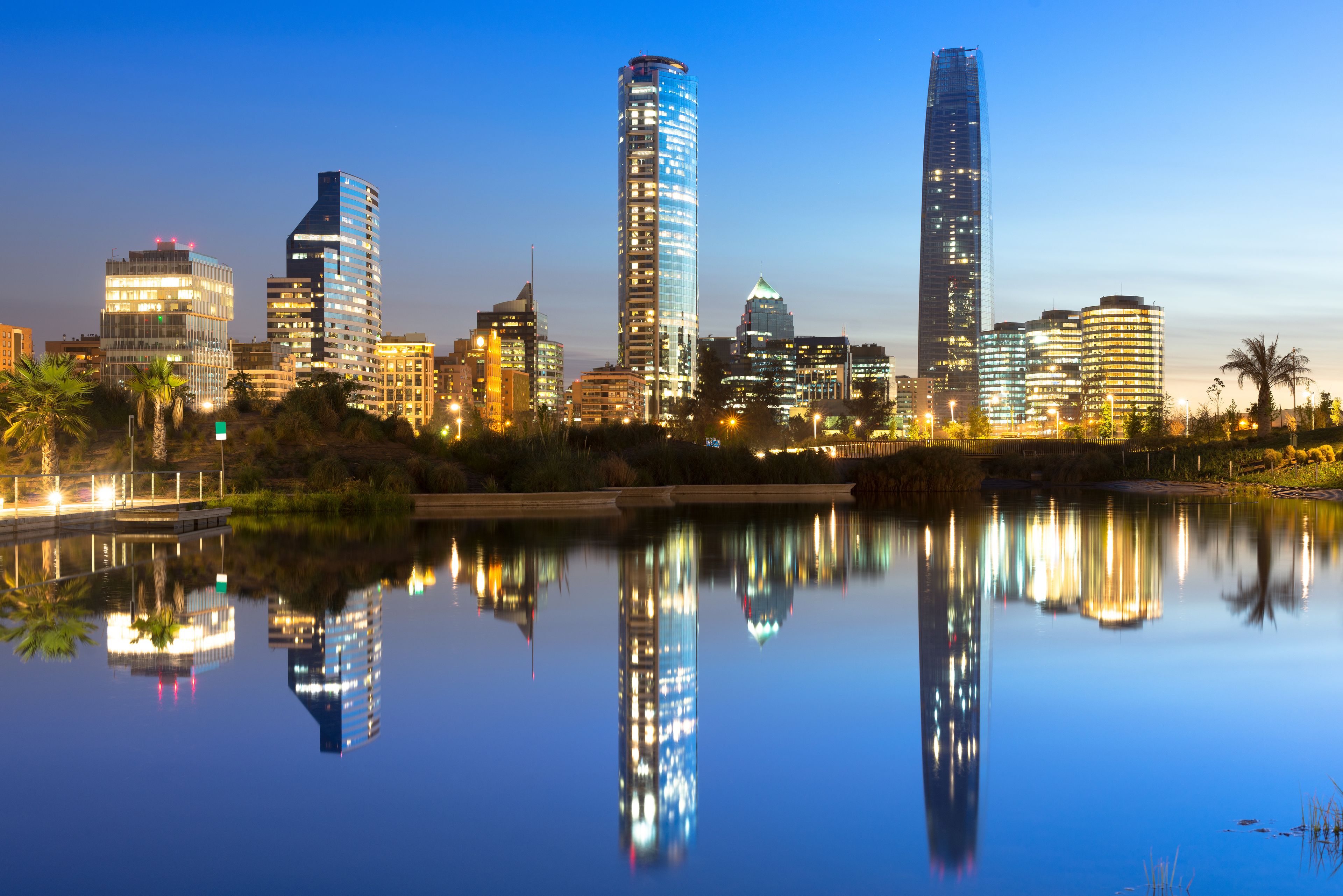 A city skyline at dusk with modern skyscrapers reflected in a calm body of water.