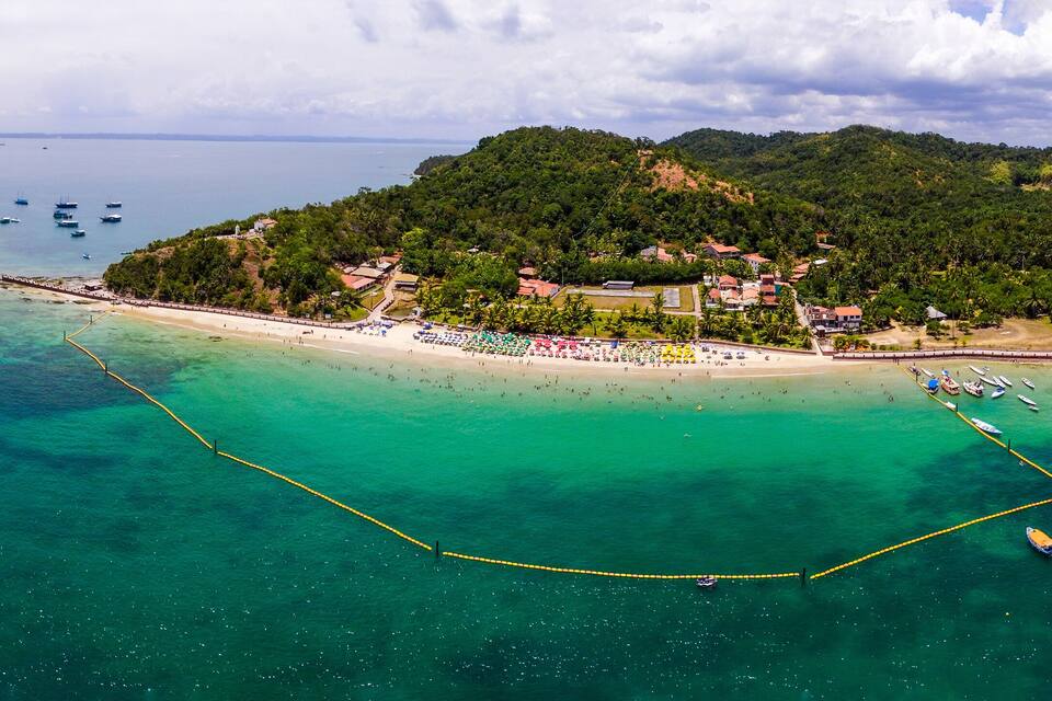 An aerial view of a tropical island with a beach, clear turquoise waters, and a pier.