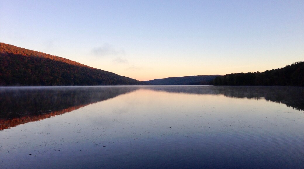 A calm lake with reflections of the surrounding forest and hills.