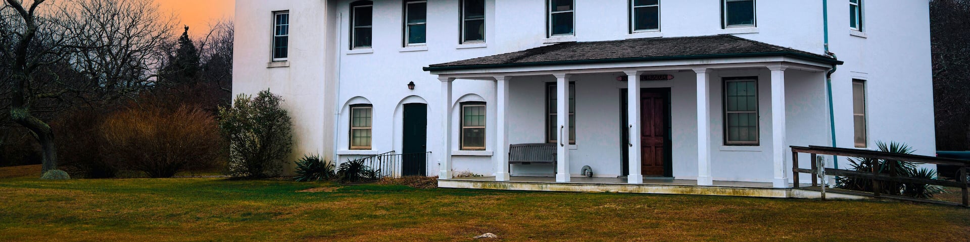 A white colonial-style house with a green roof and a lighthouse tower.