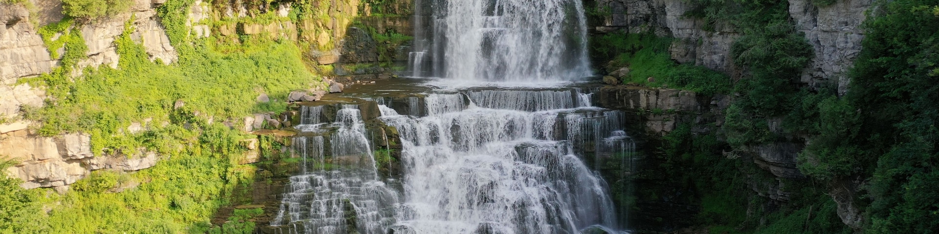Ein mehrstufiger Wasserfall, umgeben von üppiger Vegetation und felsigen Klippen.