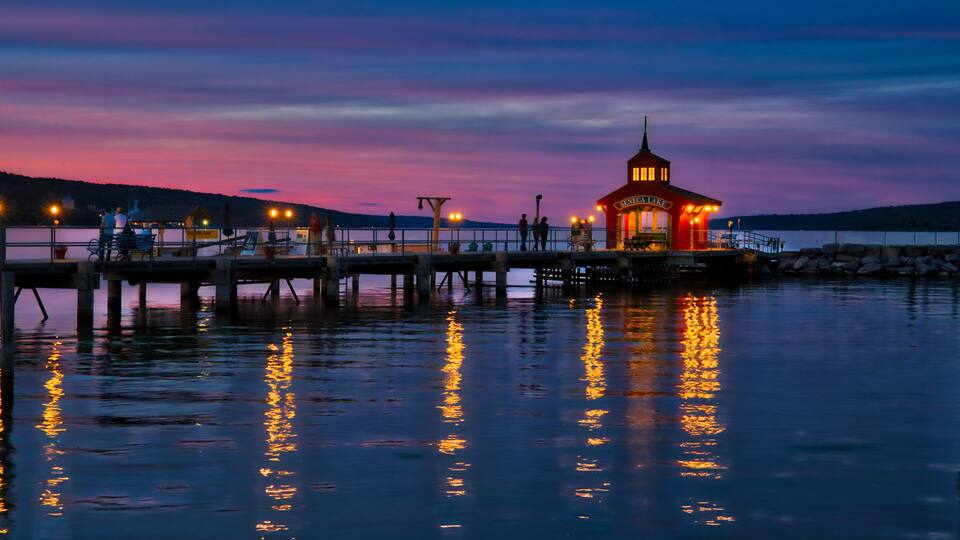 A pier with a red lighthouse at dusk, reflecting on calm water.