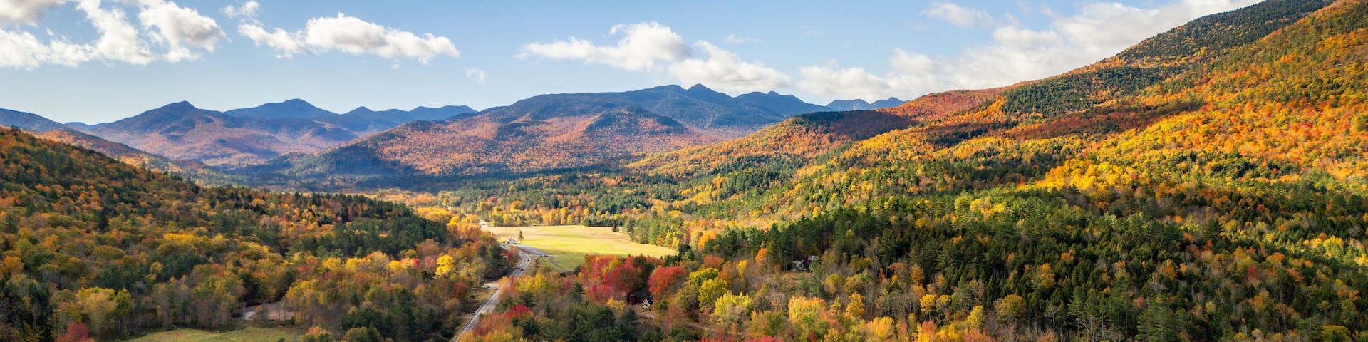 A mountainous landscape with autumn foliage, a winding road, and a clear sky.