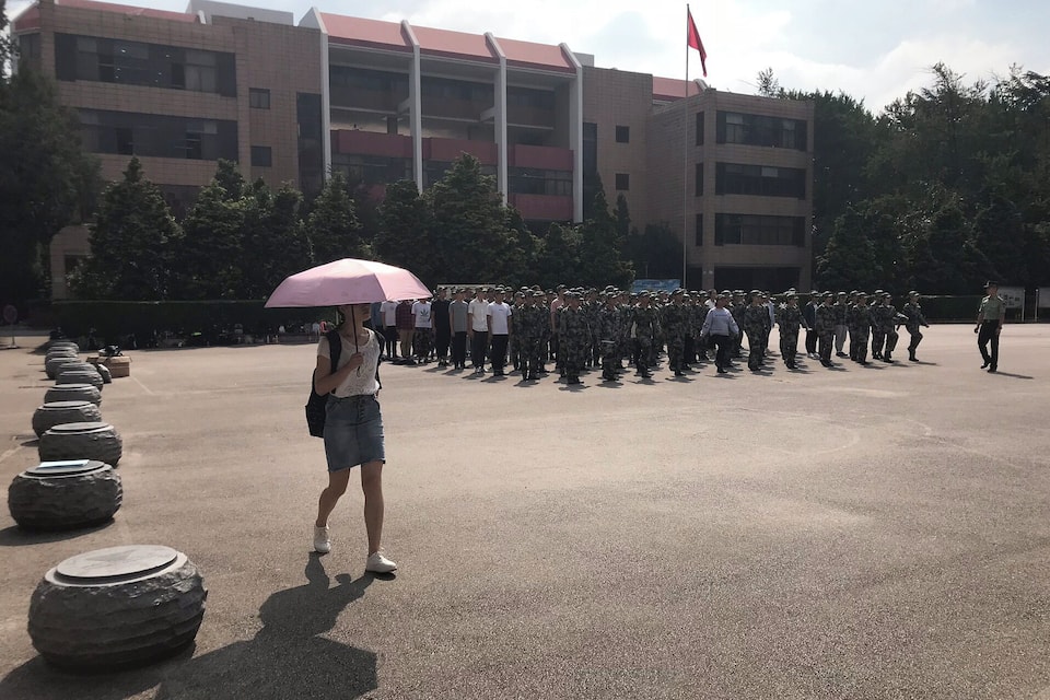 A person holding a pink umbrella in front of a building with a red flag.