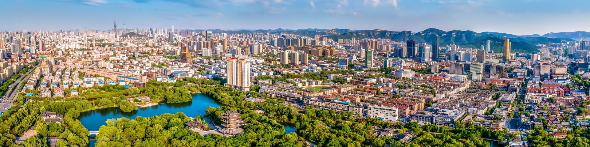 Paisagem urbana com um rio, parques verdes e montanhas ao fundo.