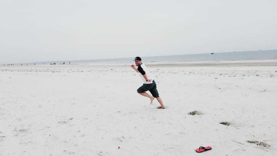 Una persona corriendo en una playa de arena con algunas chanclas y una gorra en el suelo.