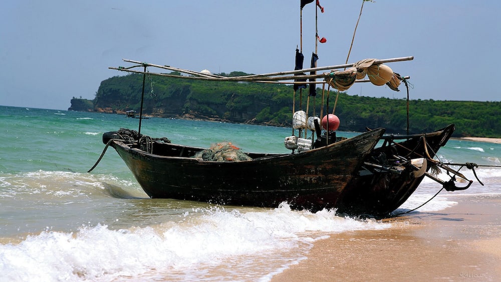 A wooden boat beached on a sandy shore with the ocean in the background.
