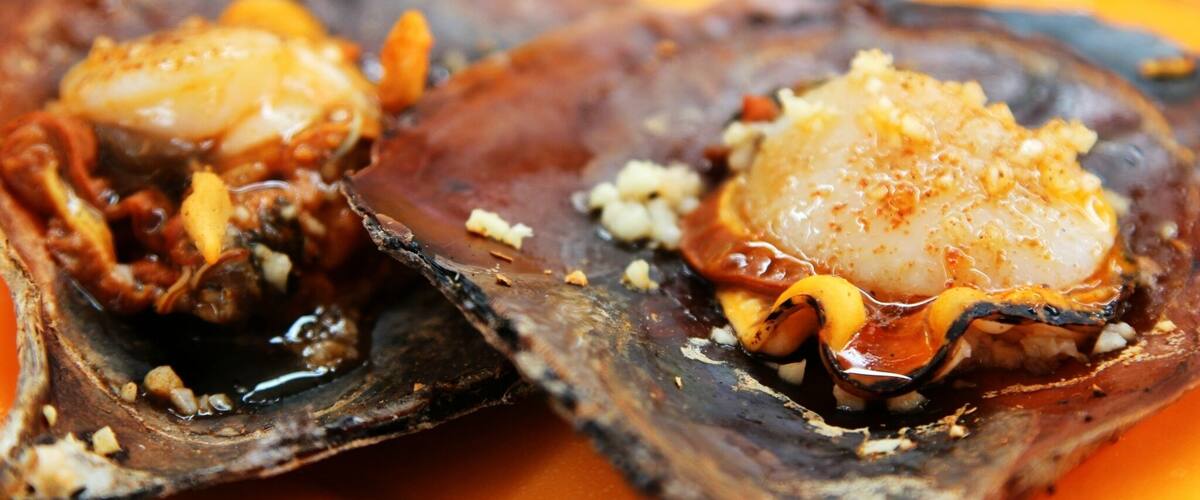Two oysters with a creamy topping and a sauce.