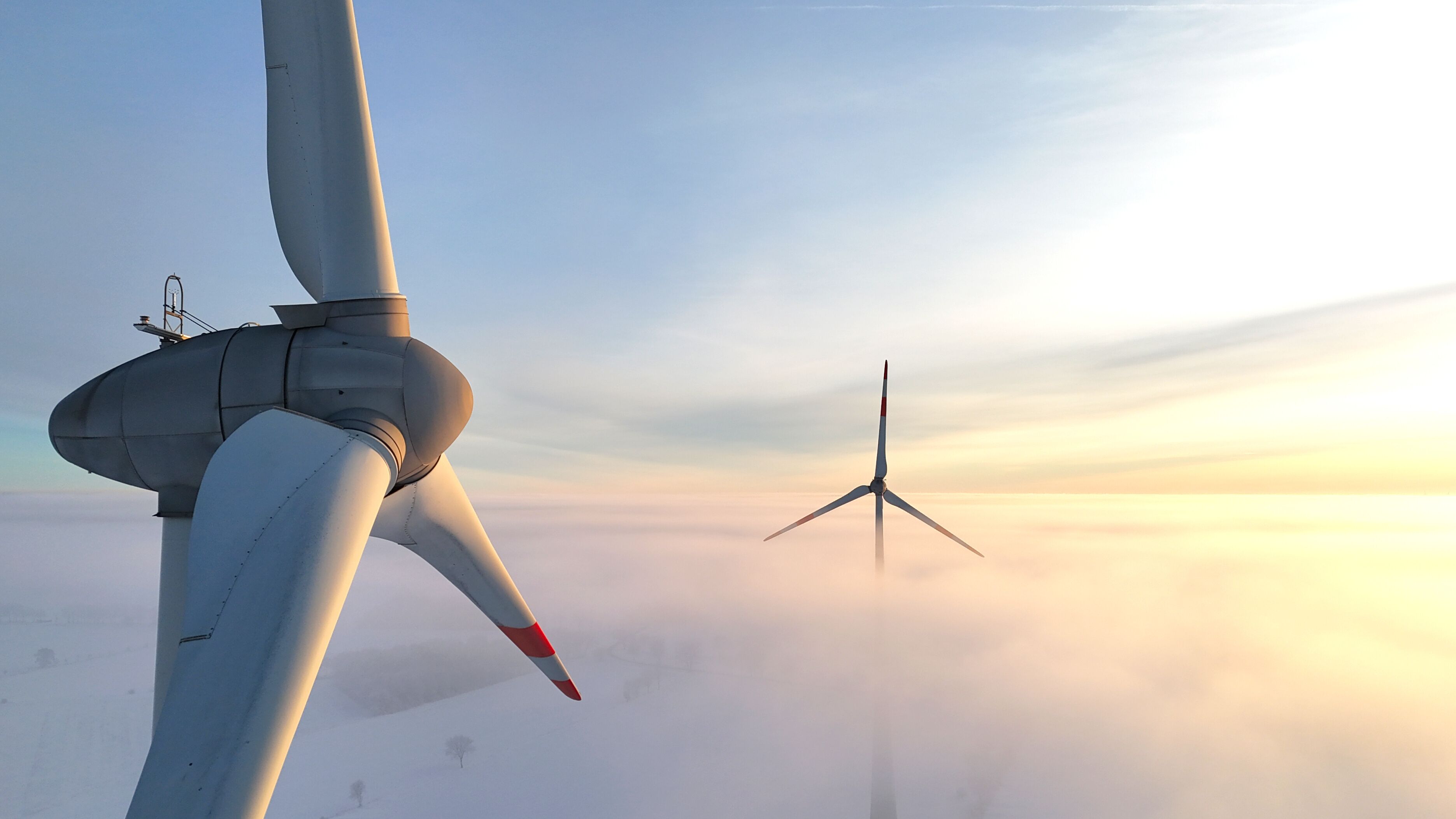 Deux éoliennes dans un paysage brumeux.