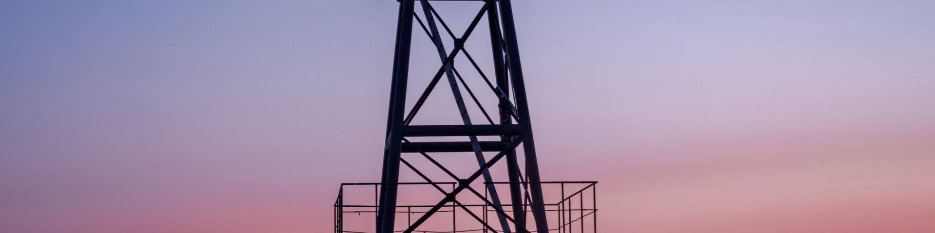 A tower stands at the end of a pier at sunrise, nestled in a tranquil atmosphere, overlooking the North Sea or Jade Bay in the morning at the cross-range light, Alte Mole in 26382 Wilhelmshaven, Germa