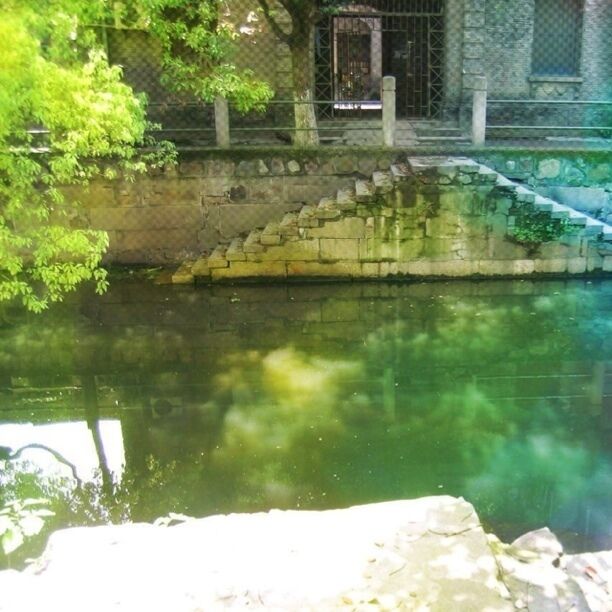 A stone bridge over a calm river, surrounded by lush greenery and a stone wall.