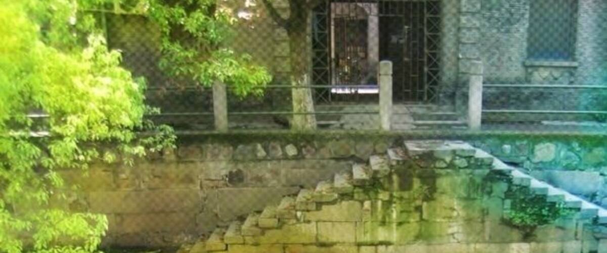 A stone bridge over a calm river, surrounded by lush greenery and a stone wall.