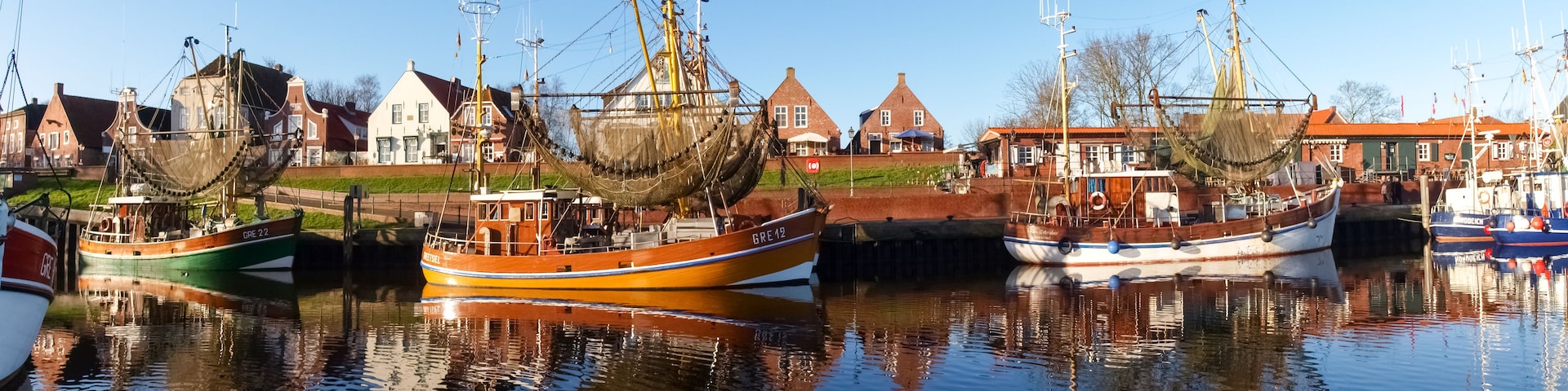 A harbor with several traditional wooden boats docked, reflecting in calm water.