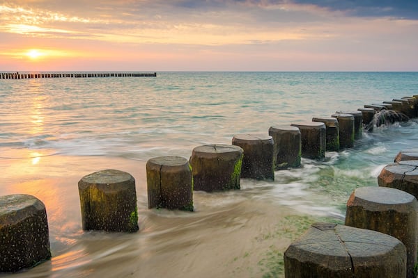 Ein Sonnenuntergang über einem ruhigen Meer mit einem hölzernen Wellenbrecher, der sich ins Wasser erstreckt.