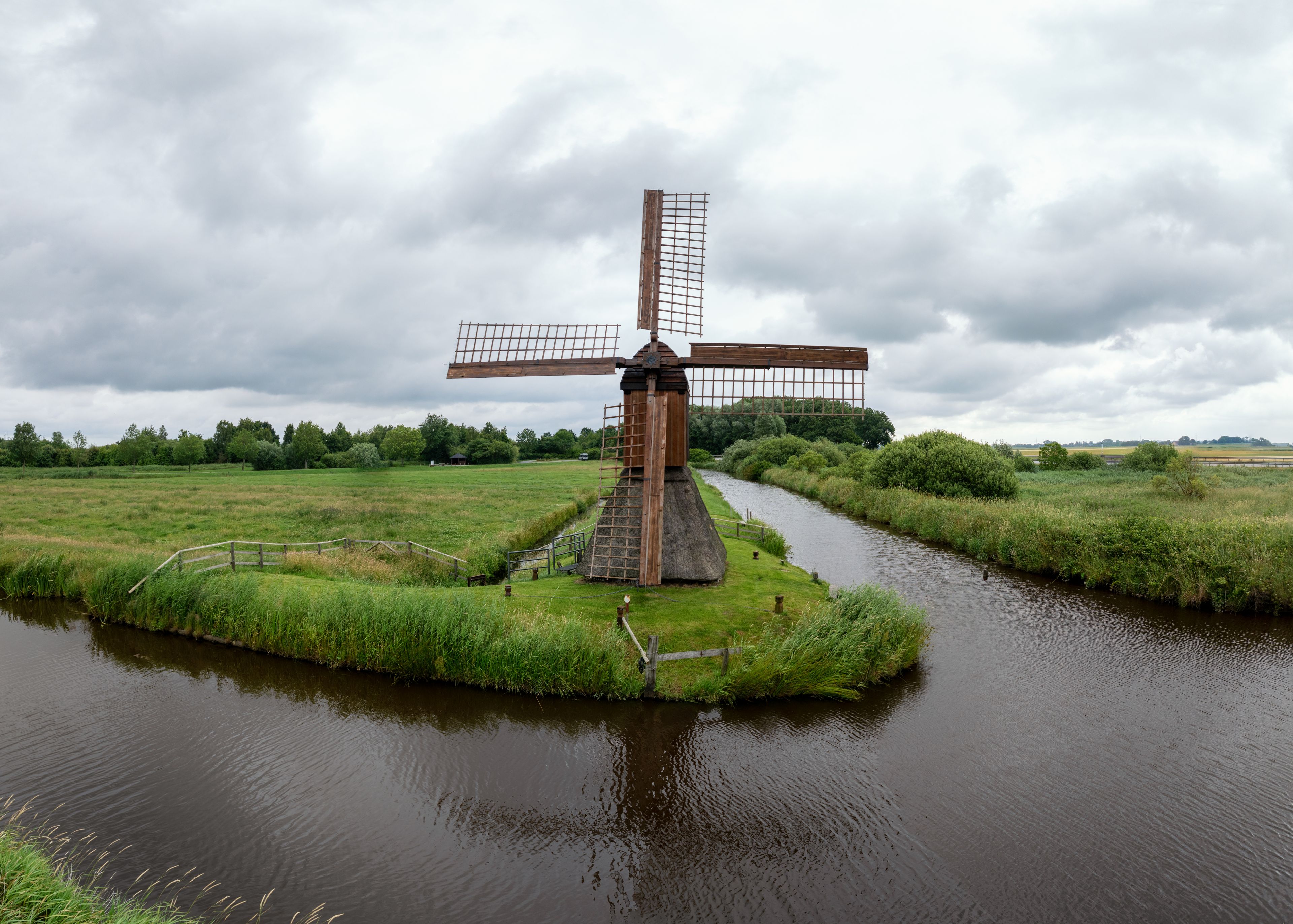 A windmill by a river with a cloudy sky.