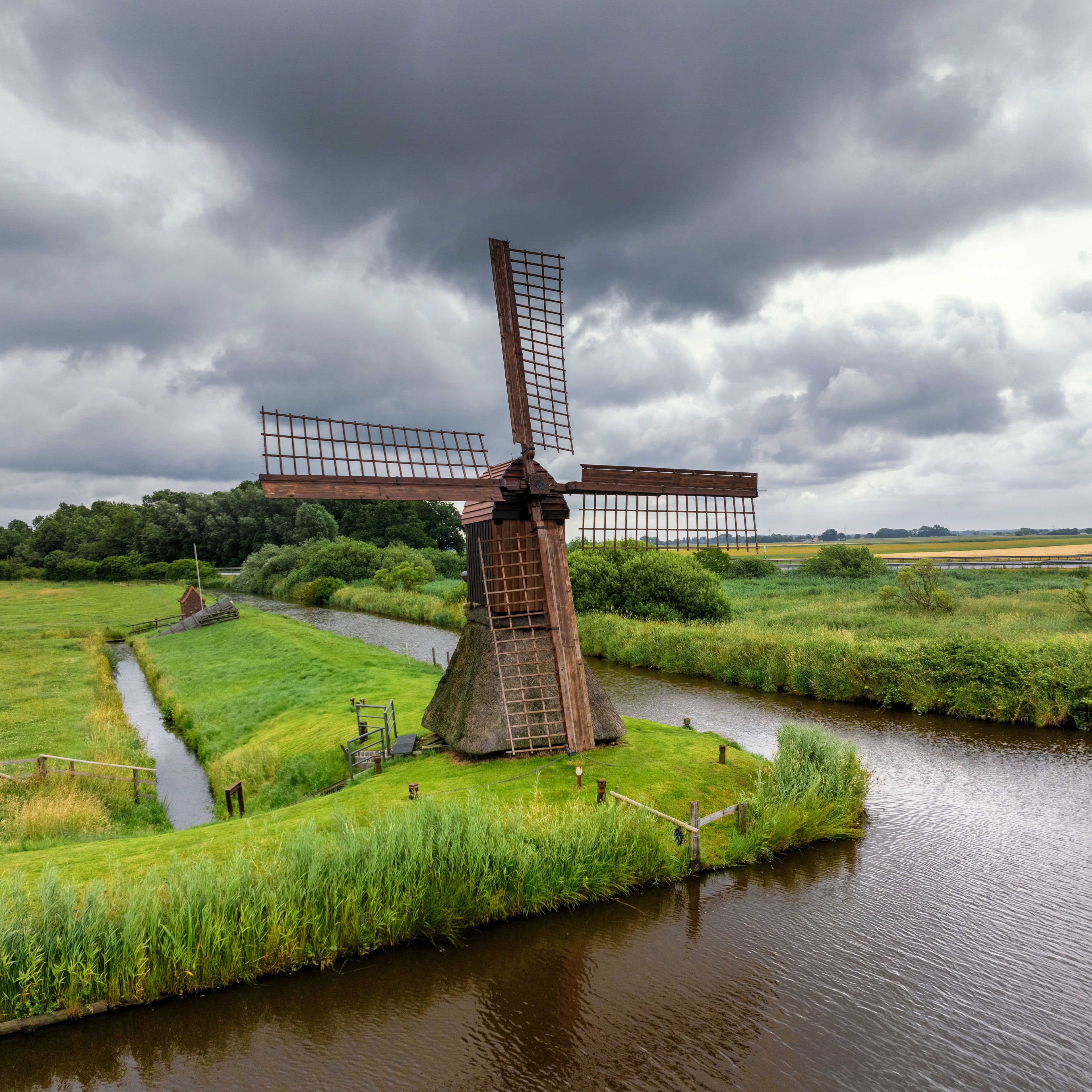 A traditional windmill in a lush green landscape with a river.
