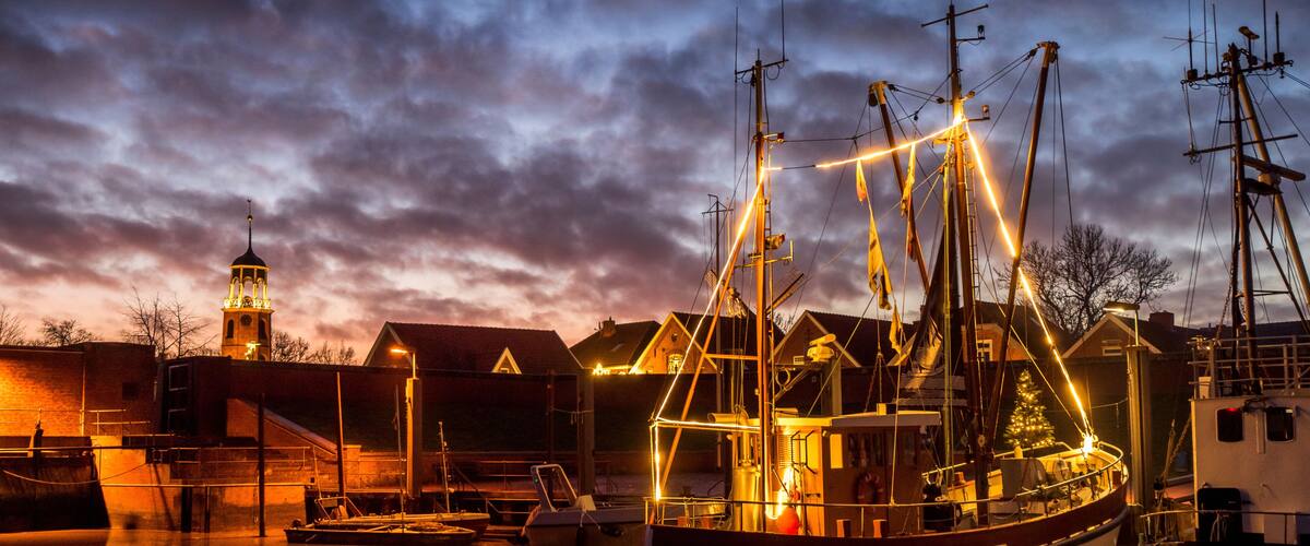 Een zeilschip in een haven, met een kerktoren op de achtergrond.