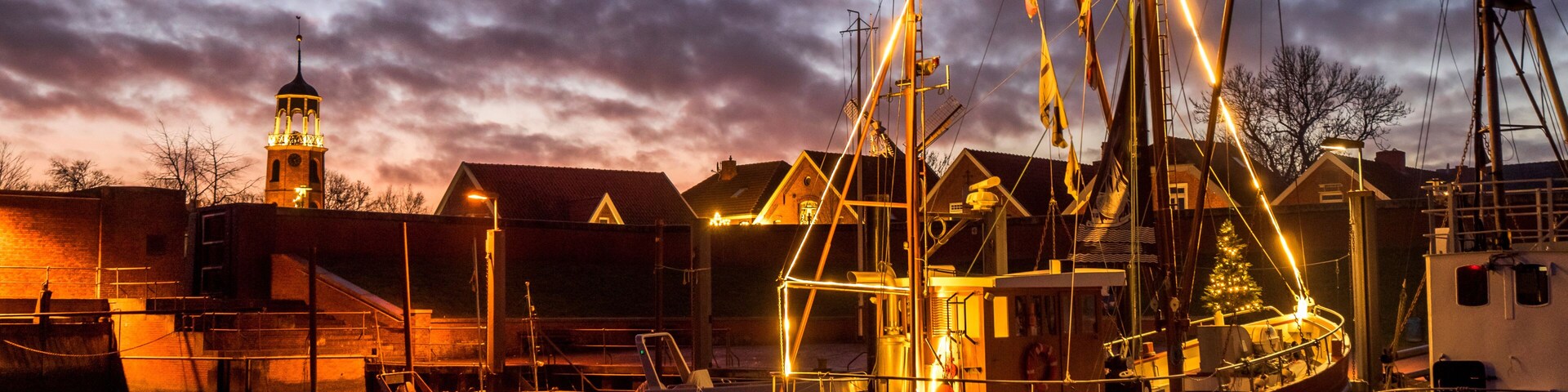 A sailing ship docked at a harbor with a church steeple in the background.