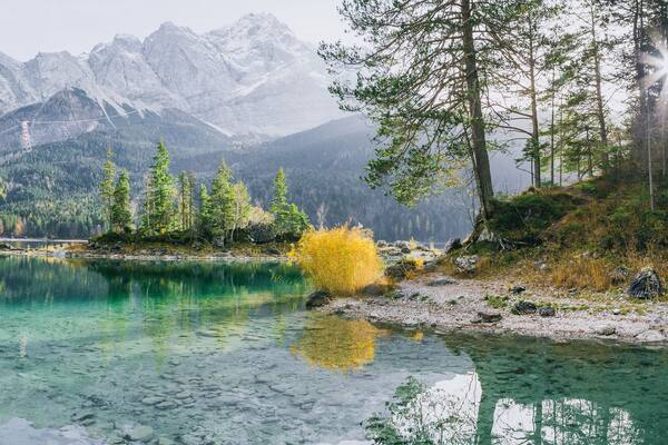 Ein klarer Bergsee, umgeben von dichtem Wald und zerklüfteten Bergen.