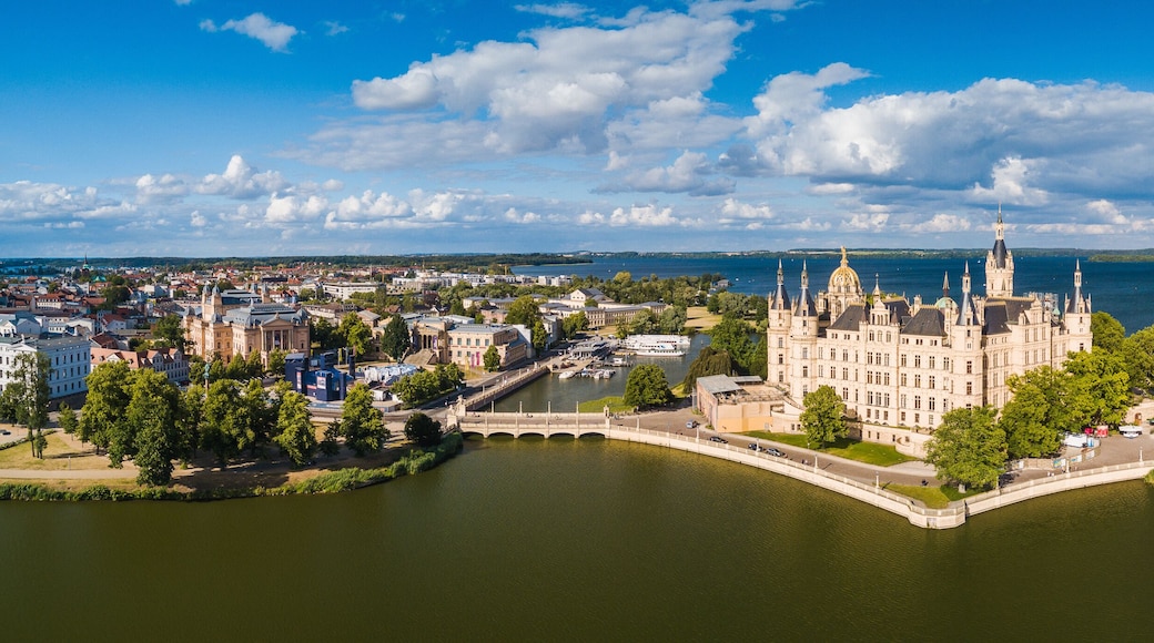 Un chĂąteau historique situĂ© au bord dâun lac, avec un pont, et entourĂ© dâune ville et de verdure.