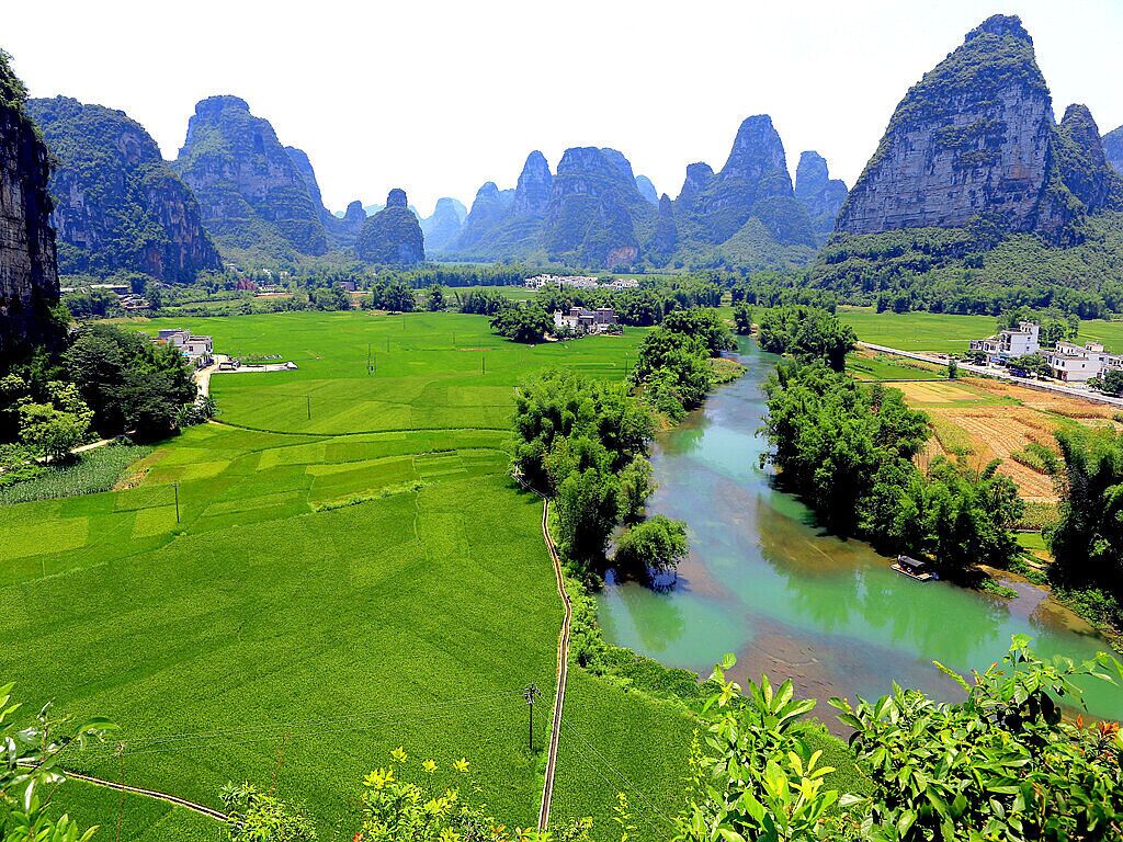 A river winding through lush green fields, surrounded by towering limestone cliffs.