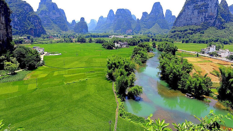 A river winding through lush green fields, surrounded by towering limestone cliffs.