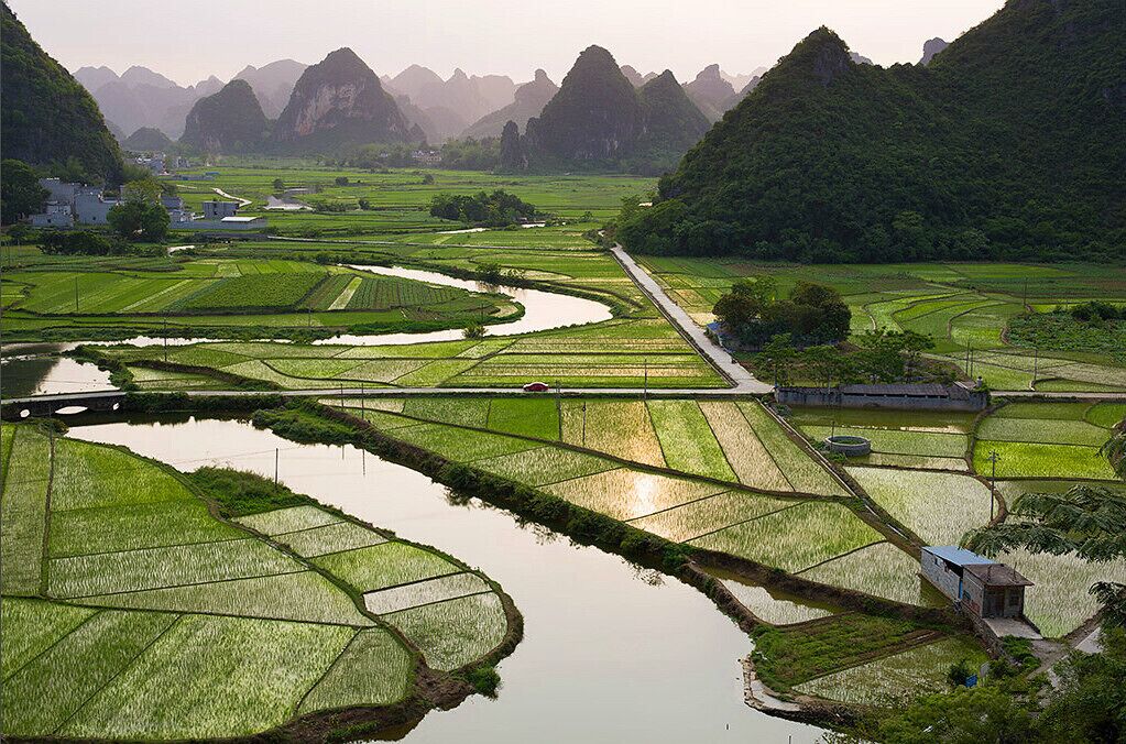 A terraced rice paddy field with a water channel, surrounded by mountains.