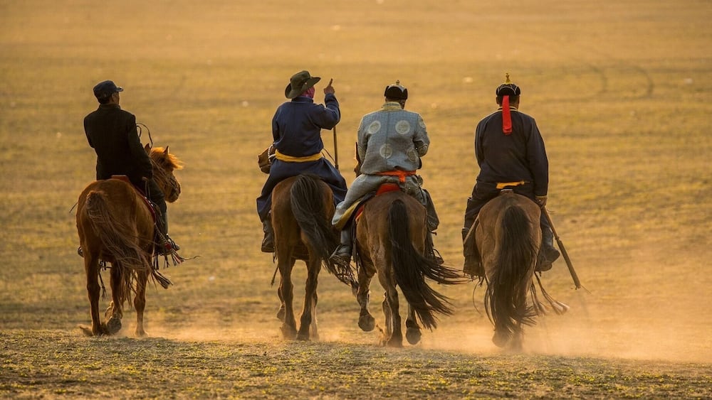 Four riders on horses in a dusty field.