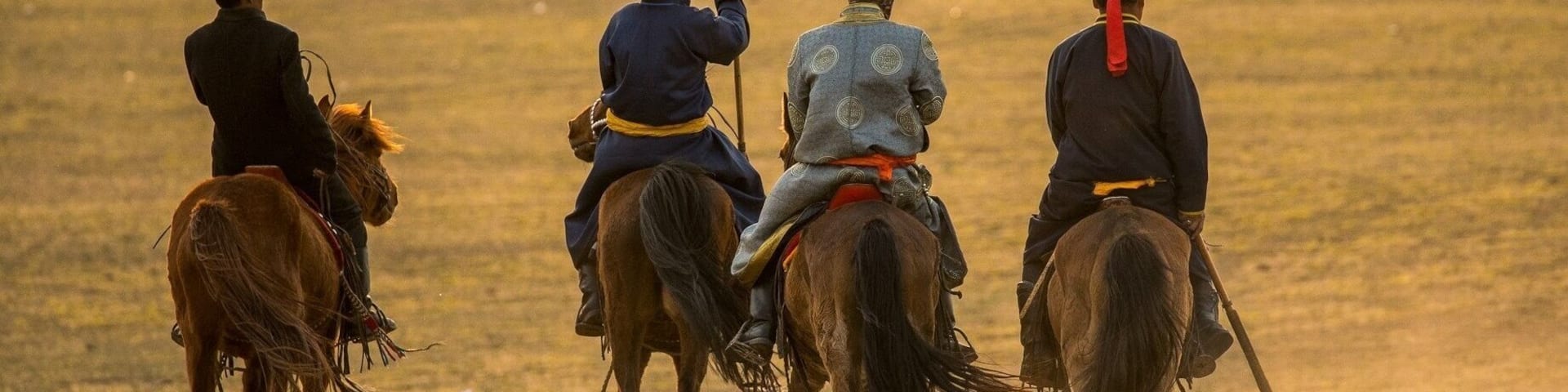 Four riders on horses in a dusty field.