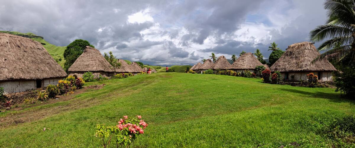 A village with thatched-roof houses, green hills, and a cloudy sky.