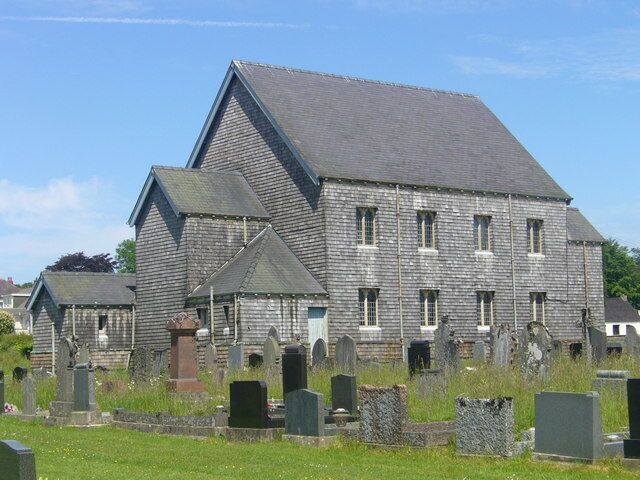 A large stone building with a steep roof, surrounded by a cemetery with numerous headstones.