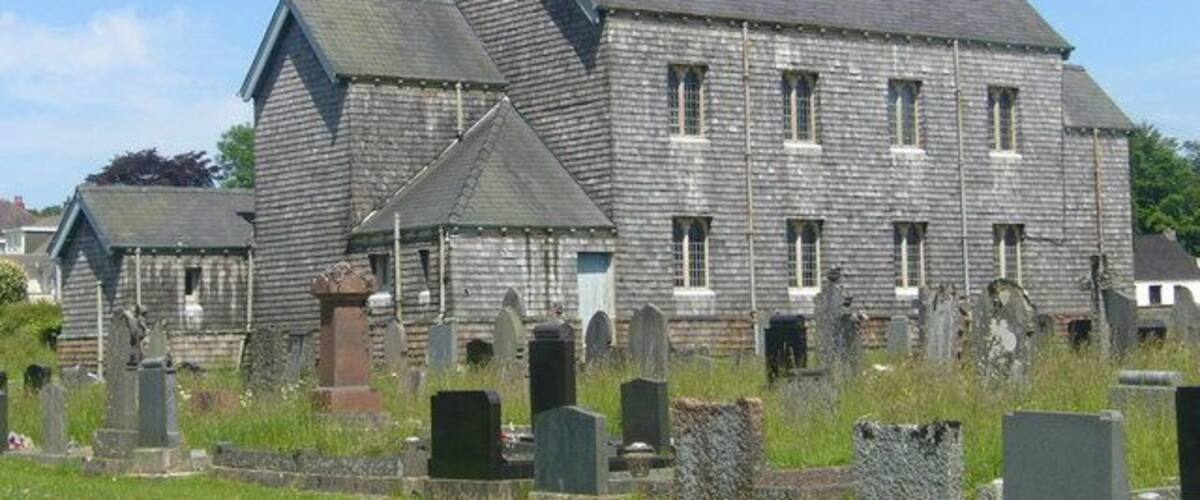 A large stone building with a steep roof, surrounded by a cemetery with numerous headstones.