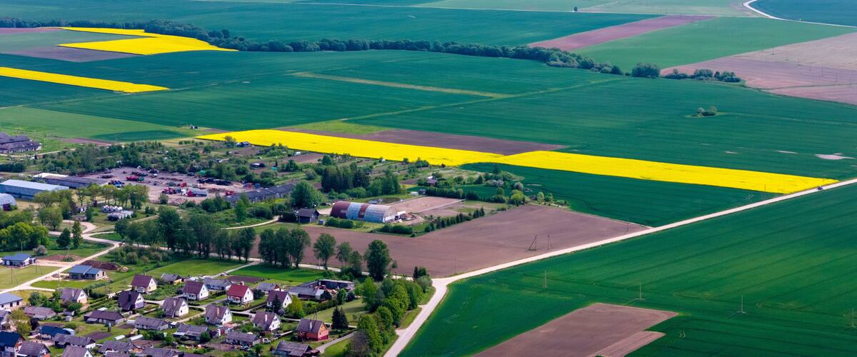 An aerial view of a rural landscape with fields of varying colors, a small village, and scattered buildings.