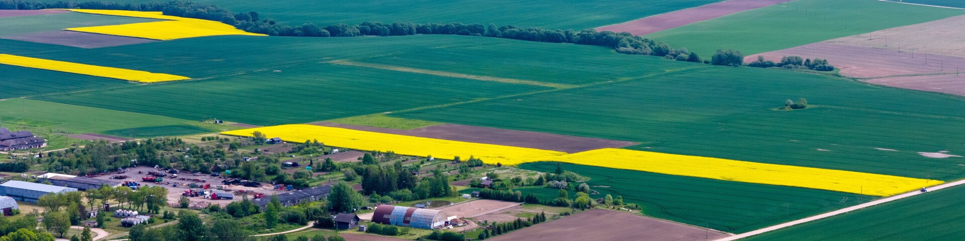 An aerial view of a rural landscape with fields of varying colors, a small village, and scattered buildings.