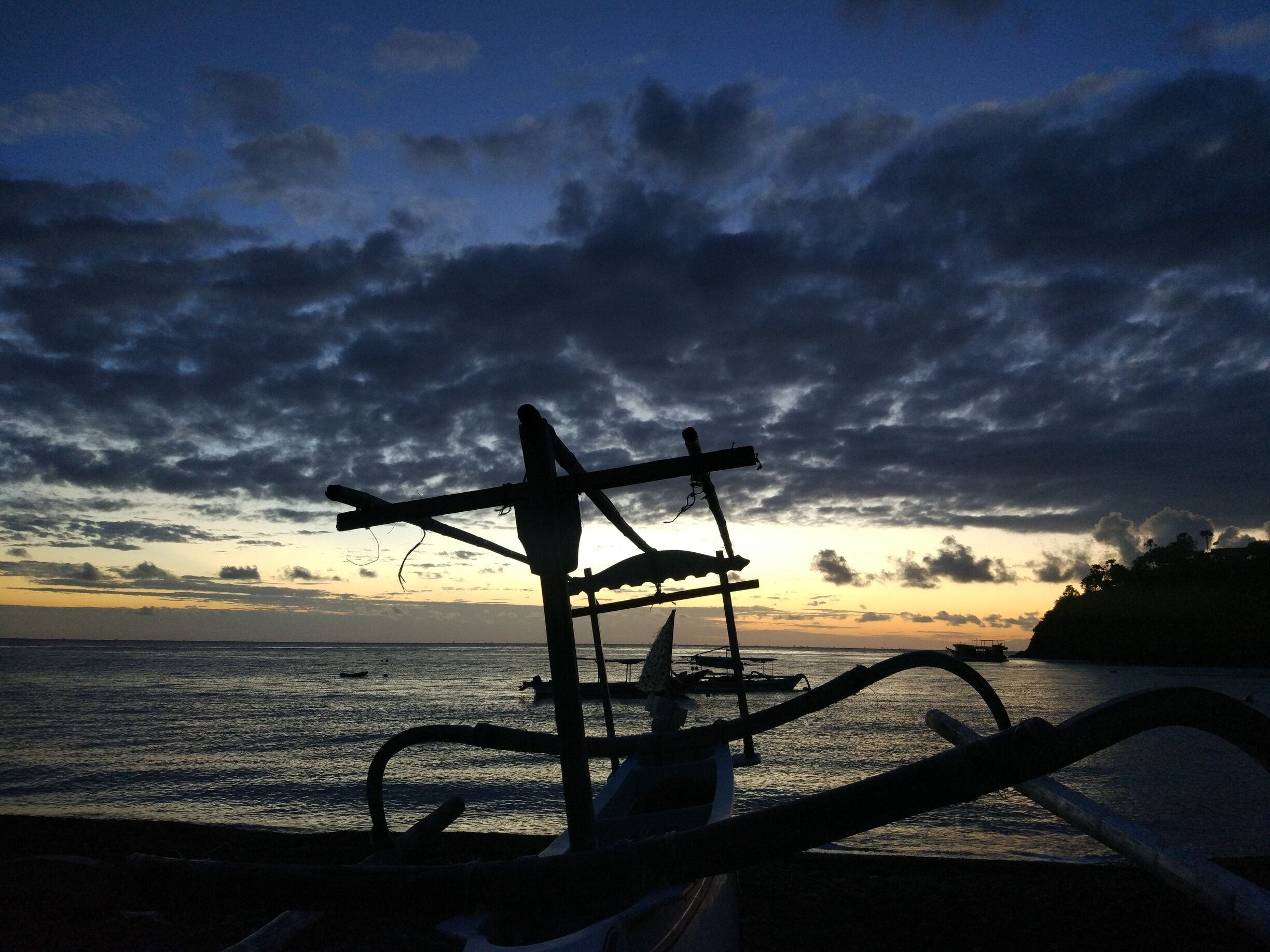 Un atardecer sobre una masa de agua con el perfil de la aparejo de un barco y un muelle en primer plano.