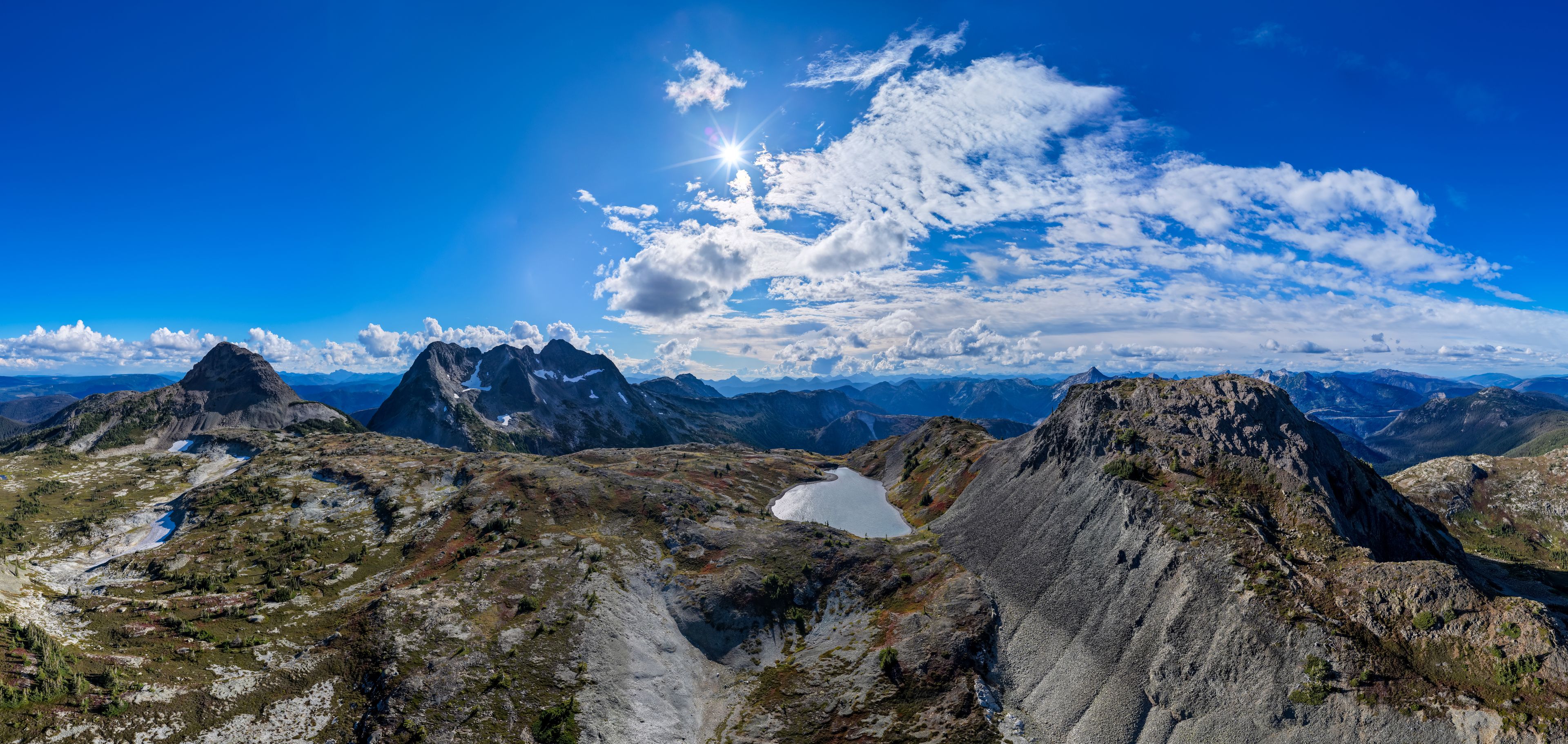 A mountain range with rugged peaks, a clear blue sky, and a small lake.