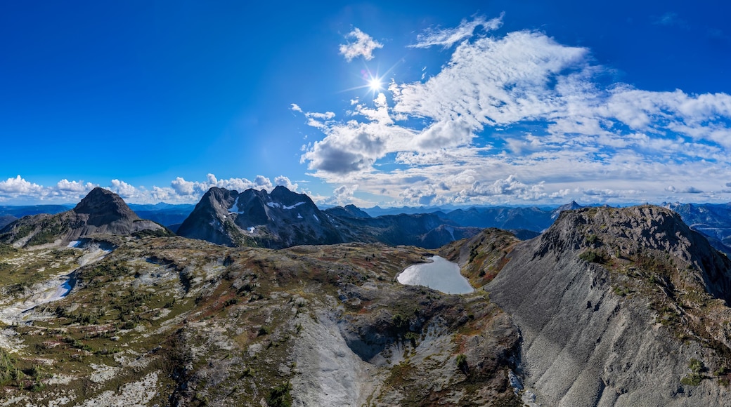 A mountain range with rugged peaks, a clear blue sky, and a small lake.