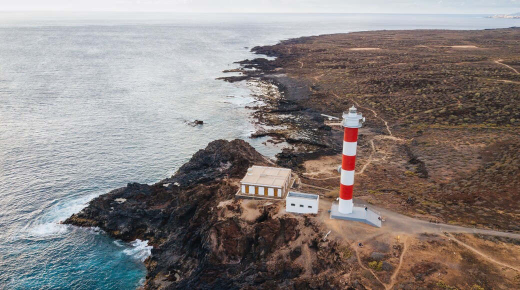 A coastal landscape with a prominent red and white lighthouse, rocky terrain, and a clear view of the ocean.