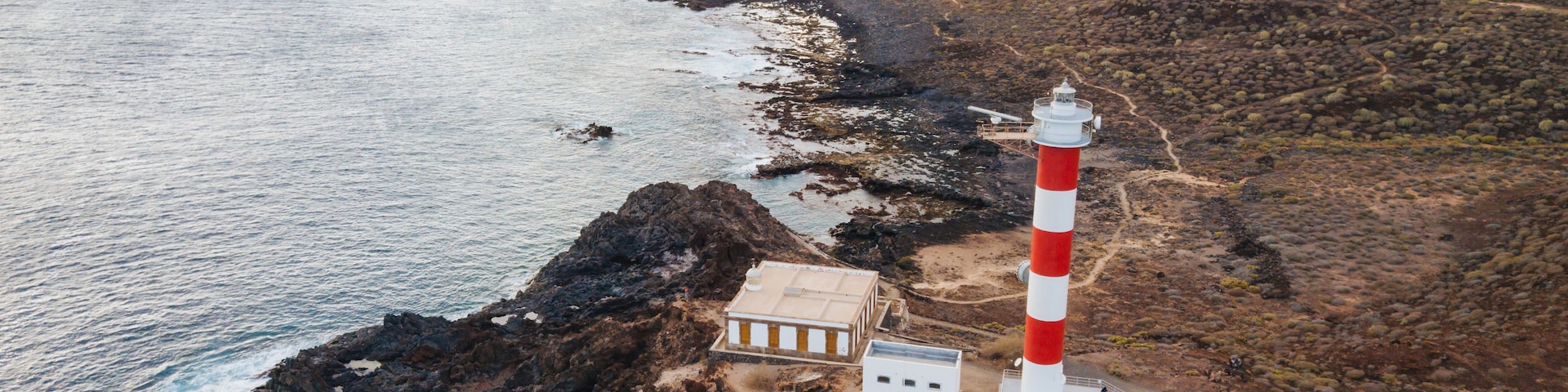 Un paisaje costero con un faro rojo y blanco destacado, terreno rocoso y una vista despejada del océano.