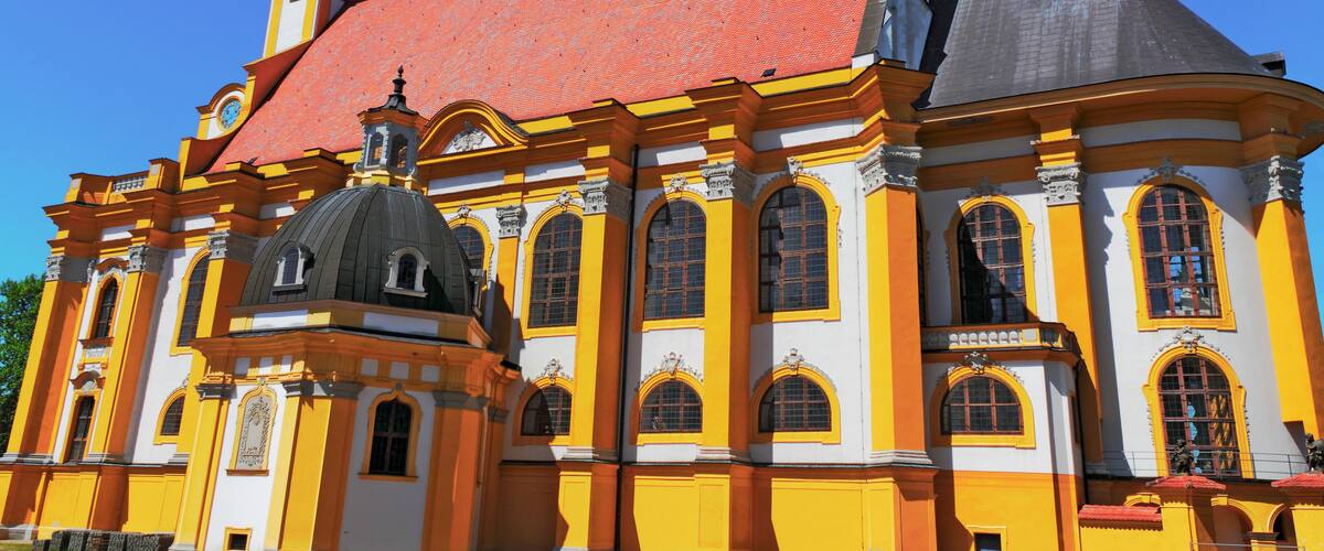 A church with a red roof, yellow and white walls, and two black spires.