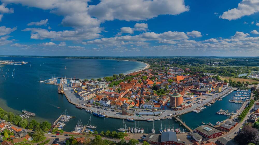 Eine Küstenstadt mit einem zentralen Hafen, umgeben von Grünflächen und einer weiten Wasserfläche.