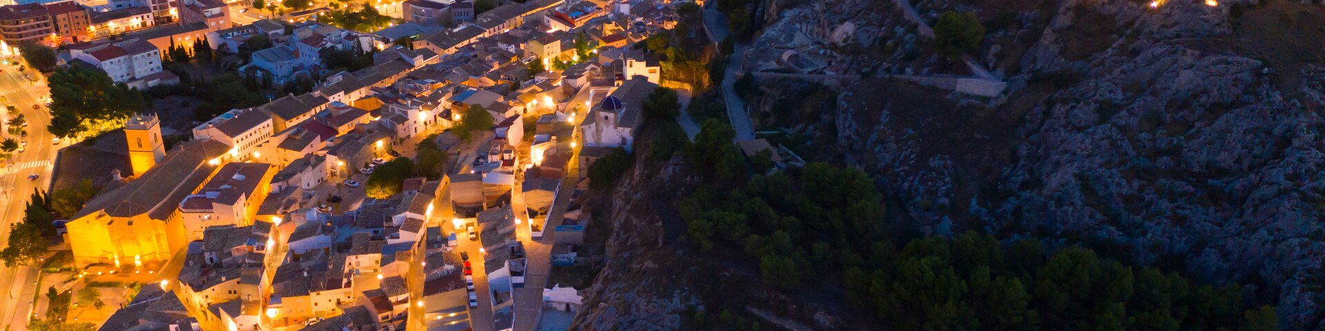 Aerial view of medieval fortified Castalla Castle on top of stone hill on background with townscape in twilight, province of Alicante, Spain..