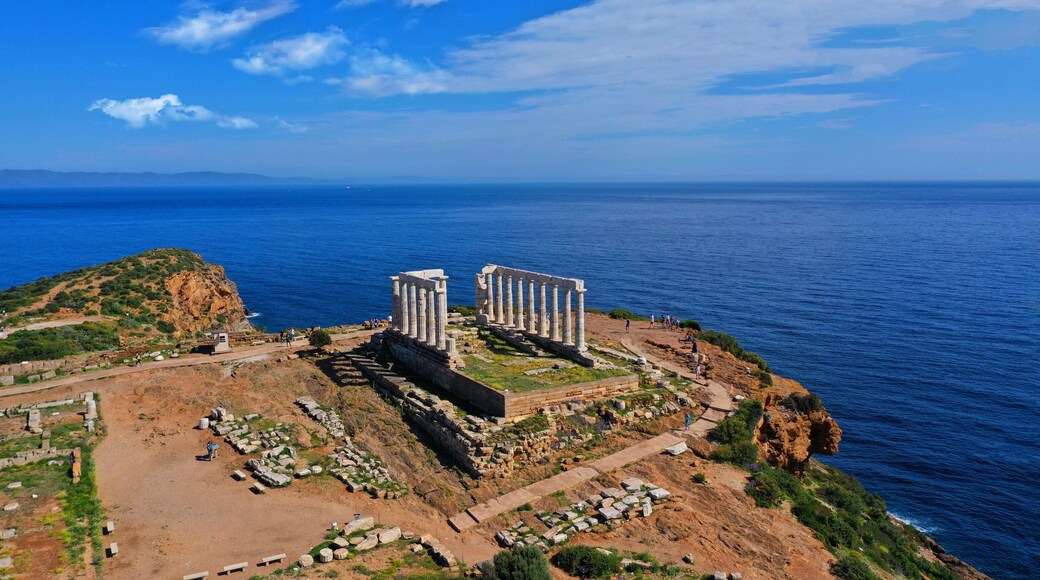 An ancient ruin with columns on a cliff overlooking the sea.