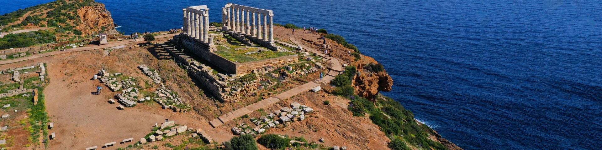 An ancient ruin with columns on a cliff overlooking the sea.