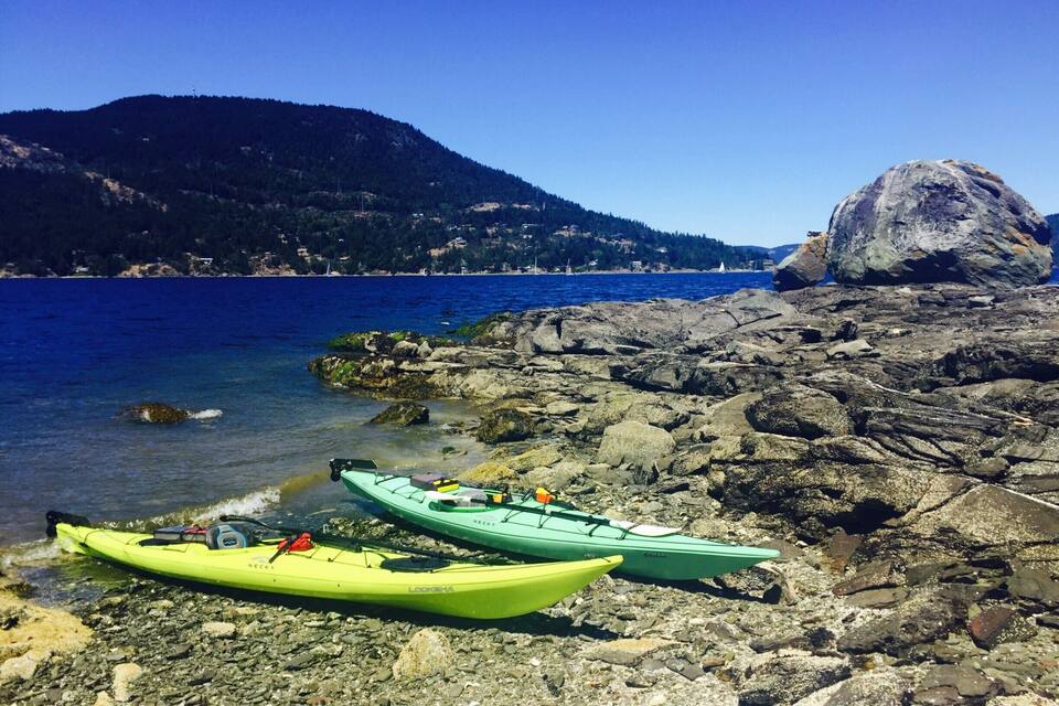 A rocky shoreline with kayaks and a large rock formation in the background.