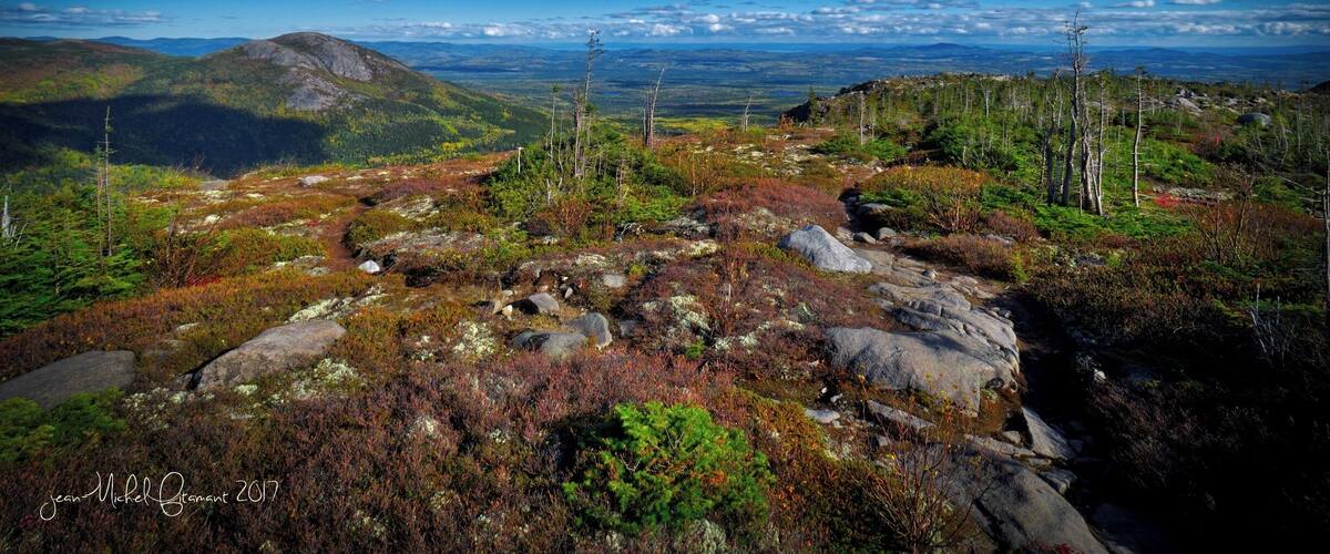 A mountainous landscape with rocky terrain, sparse vegetation, and a clear blue sky.