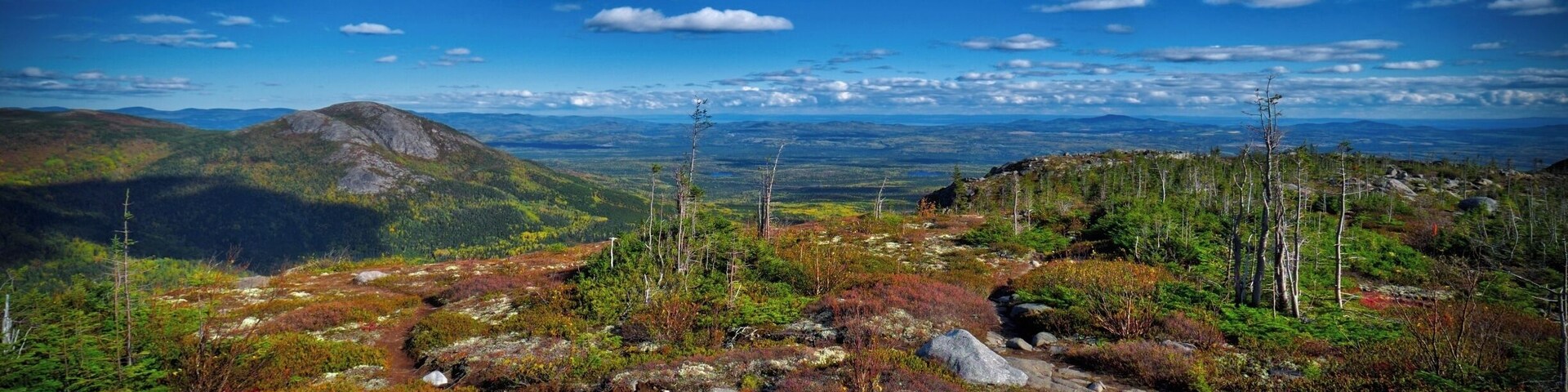 A mountainous landscape with rocky terrain, sparse vegetation, and a clear blue sky.