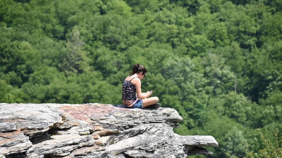 A person sitting on a rocky ledge with a forest in the background.