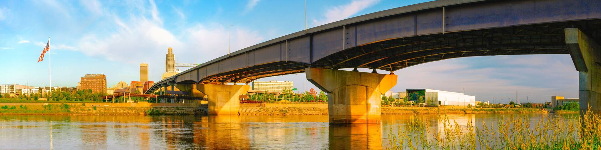 A bridge over a river with city buildings in the background.